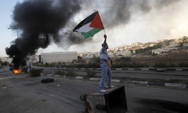 Palestinian stone-thrower holds a flag as he stands atop a garbage bin during clashes with Israeli security forces near Ramallah