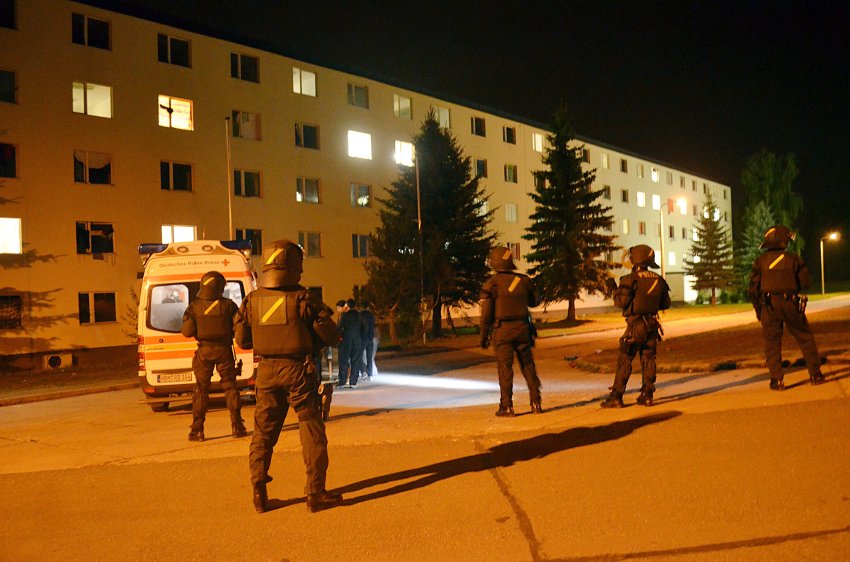 Polizeibeamte stehen am 20.08.2015 vor der Flüchtlingsunterkunft in Suhl. Vorangegangen war ein Streit zwischen Flüchtlingen in der Landeserstaufnahmestelle in Suhl am Mittwochabend, weil ein Asylbewerber mit dem Koran unflätig umgegangen sei. Bei der Auseinandersetzung wurden drei Polizeibeamte und mindestens zehn Heimbewohner verletzt. Zudem wurden sechs Polizeiautos beschädigt. Foto: Martin Wichmann/dpa +++(c) dpa - Bildfunk+++