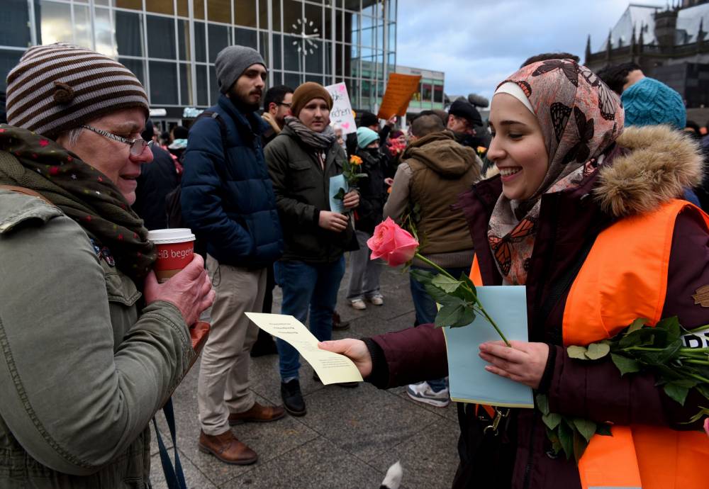 Refugees from Syria present flowers to passers-by as they demonstrate against violence near the Cologne main train station in Cologne, western Germany on January 16, 2016, where hundreds of women were groped and robbed in a throng of mostly Arab and North African men during New Year's festivities. German authorities said that nearly all the suspects in a rash of New Year's Eve violence against women in Cologne were "of foreign origin", as foreigners came under attack amid surging tensions. / AFP / PATRIK STOLLARZPATRIK STOLLARZ/AFP/Getty Images